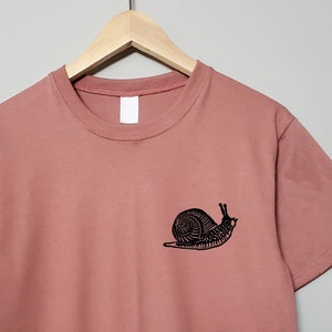 May include: A dusty rose t-shirt with a black snail graphic on the left chest.