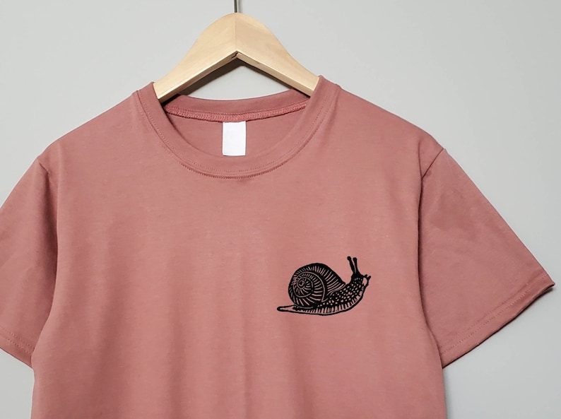 May include: A dusty rose t-shirt with a black snail graphic on the left chest.