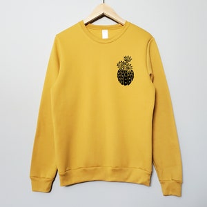 May include: A mustard yellow sweatshirt with a black graphic of a pineapple on the front.