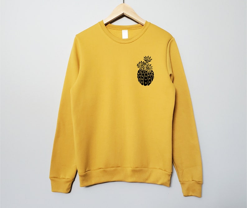 May include: A mustard yellow sweatshirt with a black graphic of a pineapple on the front.