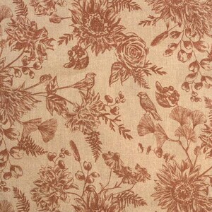 May include: A beige fabric with a brown floral pattern. The pattern includes sunflowers, roses, leaves, and birds. The fabric has a textured surface.