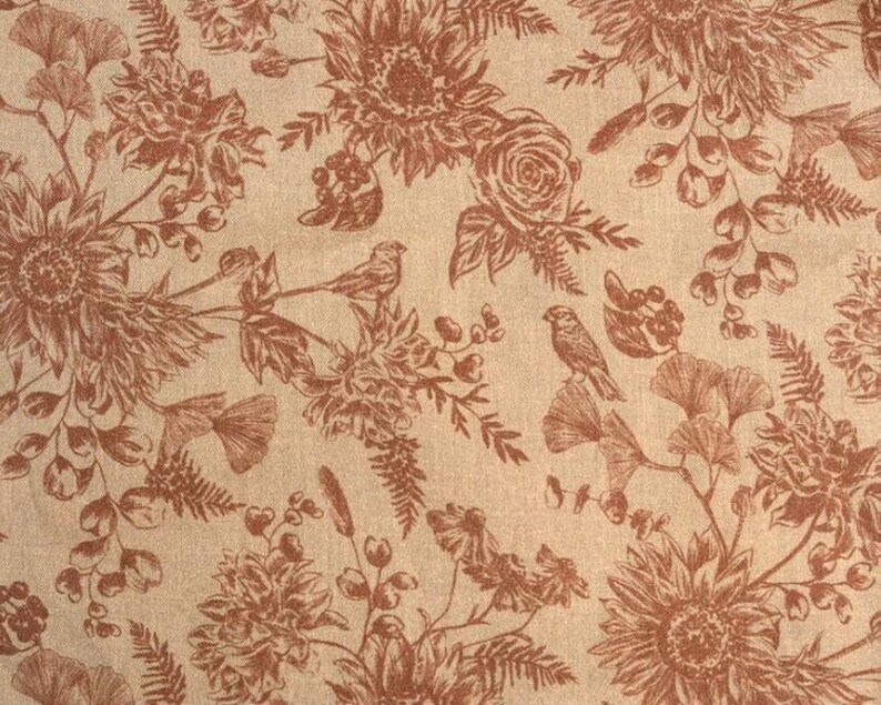 May include: A beige fabric with a brown floral pattern. The pattern includes sunflowers, roses, leaves, and birds. The fabric has a textured surface.