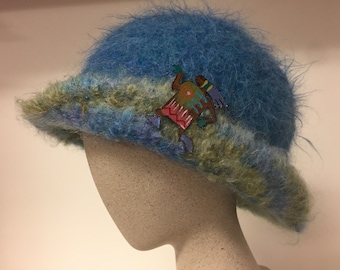 May include: A blue and green fuzzy hat with a colorful embroidered design. The hat is on a mannequin head.