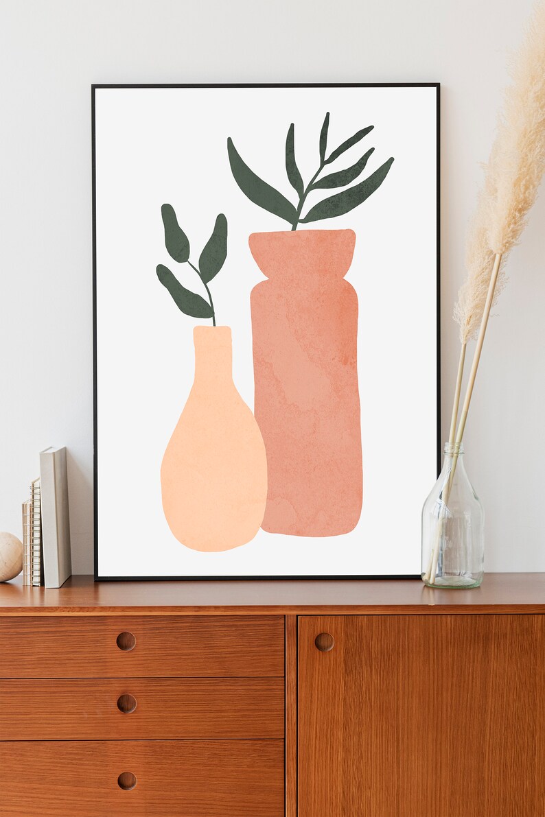 May include: A framed print of a minimalist illustration of two vases with green leaves. The vases are peach and terracotta colored and are on a white background.