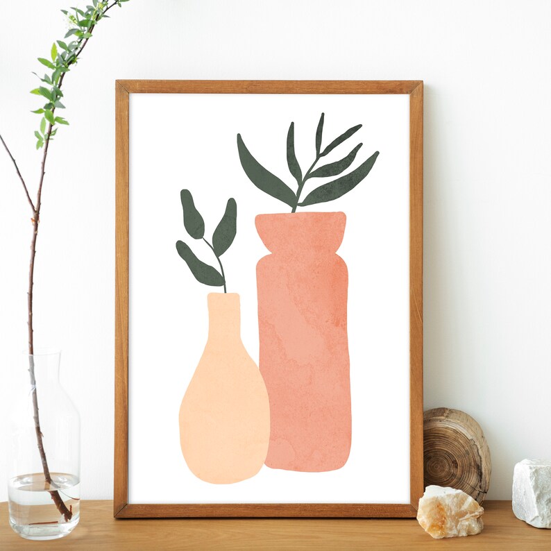 May include: A framed print of a minimalist illustration featuring two vases with green leaves. The vases are peach and pink and are set against a white background.