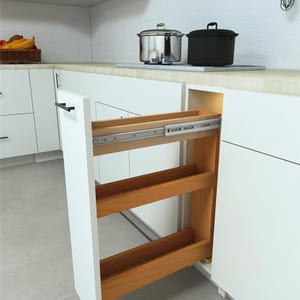 May include: A white kitchen cabinet with a pull-out spice rack. The rack has three wooden shelves and is mounted on metal tracks. The cabinet is open, revealing the interior. Stainless steel pots and pans are on the countertop.