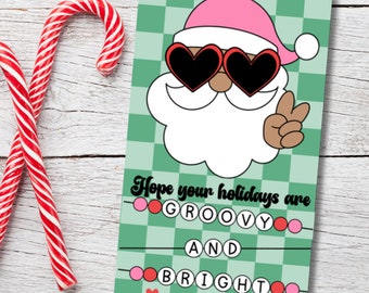 Könnte beinhalten: Eine Weihnachtskarte mit einem Cartoon-Weihnachtsmann mit herzförmiger Sonnenbrille und rosa Hut, der ein Friedenszeichen gibt. Die Karte hat einen grün karierten Hintergrund und den Text "Hope your holidays are GROOVY AND BRIGHT."