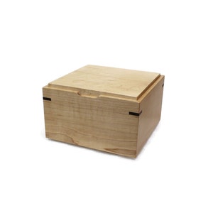 May include: A wooden box with a light wood finish and black accents. The box has a hinged lid and is made of solid wood.