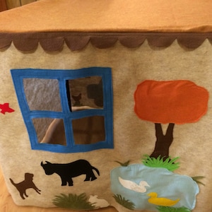 May include: A felt play tent with a brown roof, a blue window, a red bird, a brown tree with an orange leaf, a black cow, a brown dog, a white duck, and a yellow duck.