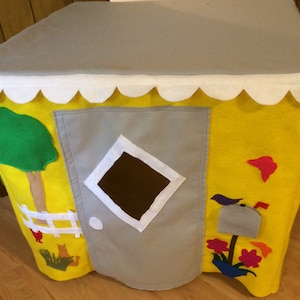 May include: A yellow felt play tent with a gray felt door, a white window, and various felt appliques including a tree, a bird, a mailbox, and flowers. The tent has a white scalloped edge.