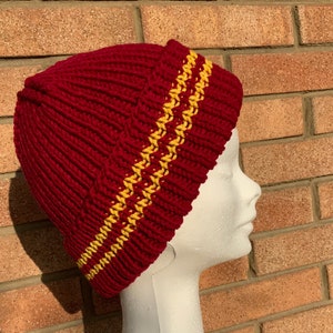 Könnte beinhalten: Eine rote Strickmütze mit zwei gelben Streifen am Rand.