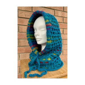 May include: A teal blue knitted hooded cowl with a colourful striped pattern around the neck opening. The cowl is made with a textured stitch and has a long, flowing tie.