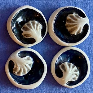 May include: Four ceramic buttons with a black and white design. Each button features a stylized white leaf design on a black background.
