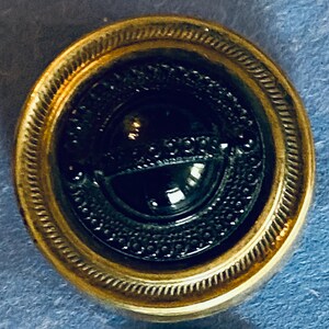 May include: A gold-coloured button with a black glass centre. The centre has a raised design with a circle and a line.