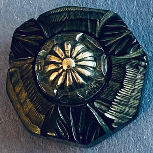 May include: A silver-toned button with a raised, flower-shaped design. The button has a textured, geometric pattern around the edges.