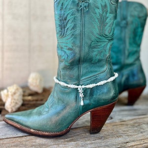 May include: Teal leather cowboy boots with a white pearl ankle bracelet and a crystal pendant.
