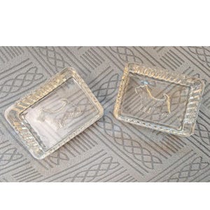 May include: Two rectangular clear glass trays featuring a molded relief of a Scottish Terrier dog in the center. Each tray has a decorative ribbed border along the edges, providing a textured appearance to the transparent glass construction.
