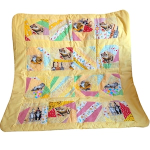 May include: A rectangular patchwork quilt featuring a yellow border and a grid of squares. Each square contains various fabric patterns in shades of yellow, pink, green, and blue, with printed illustrations of cats in various poses and settings.