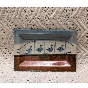 May include: A rectangular ceramic tray featuring a tri-color glaze design. The top section is a muted blue-gray, the middle is a cream band with four hand-painted black geese, and the bottom section is a textured, deep reddish-brown glaze.