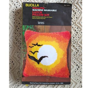 May include: A Bucilla Deluxe Pile Latch Pillow Kit, "Sanctuary" design. The pillow kit features a sunset design with birds in shades of orange, yellow, and red. The pillow measures 15 x 15 inches.