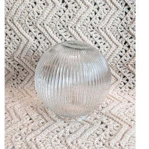 May include: A clear glass globe light shade featuring a vertical ribbed texture. The spherical lamp cover is constructed from transparent glass with a series of parallel lines running from the top to the bottom, creating a distinct linear pattern.