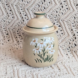 May include: A white ceramic mug with a black handle and the text "But First, Coffee" in a bold, black font. The mug is filled with a dark liquid, likely coffee, and sits on a light-colored surface.