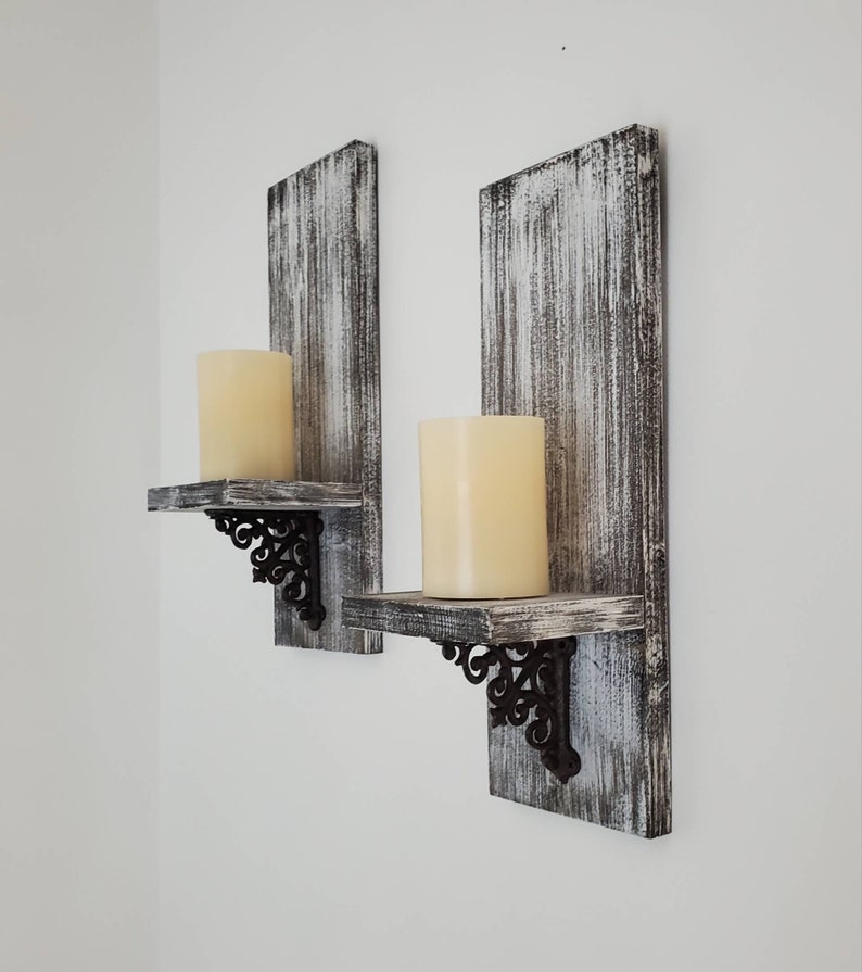 Peut inclure: Deux bougeoirs muraux rustiques. Chacun pr&eacute;sente un panneau arri&egrave;re en bois blanc et gris vieilli, une petite &eacute;tag&egrave;re et un support d&eacute;coratif en m&eacute;tal noir. Une grande bougie pilier cr&egrave;me est pos&eacute;e sur chaque &eacute;tag&egrave;re.