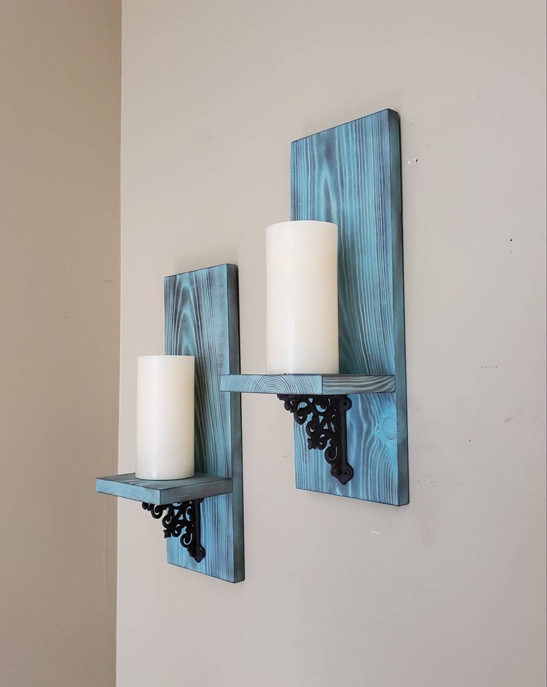 Peut inclure: Deux bougeoirs muraux avec une finition bleu vieilli. Chaque support comporte une petite &eacute;tag&egrave;re soutenue par des supports m&eacute;talliques noirs orn&eacute;s. Des bougies piliers blanches reposent sur les &eacute;tag&egrave;res, cr&eacute;ant un affichage d&eacute;coratif rustique.