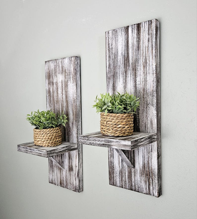 May include: Two rustic whitewashed wooden shelves with small potted plants. The shelves are mounted on a wall and have a distressed look.
