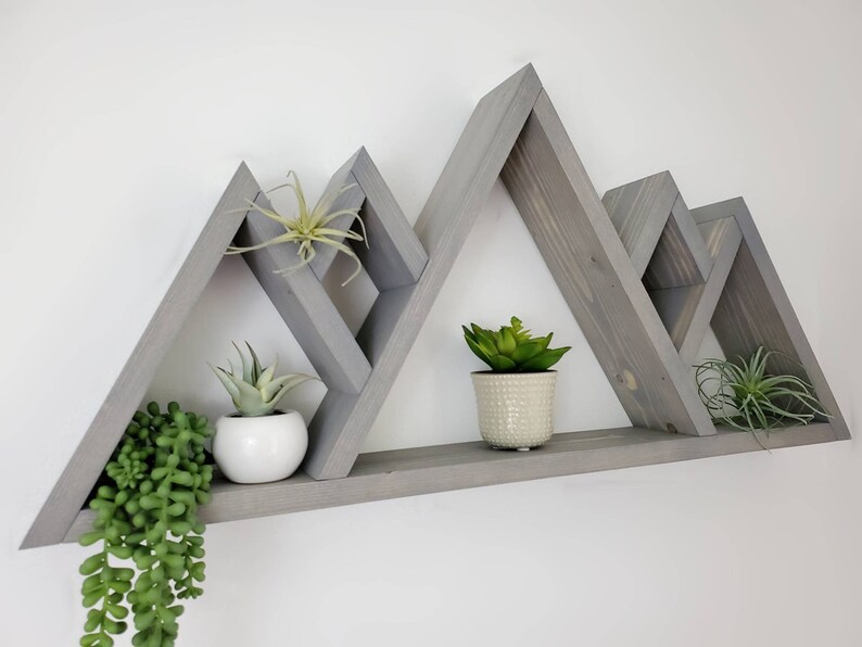 May include: Gray wooden mountain-shaped shelf with three triangular shelves. The shelf is decorated with potted plants.