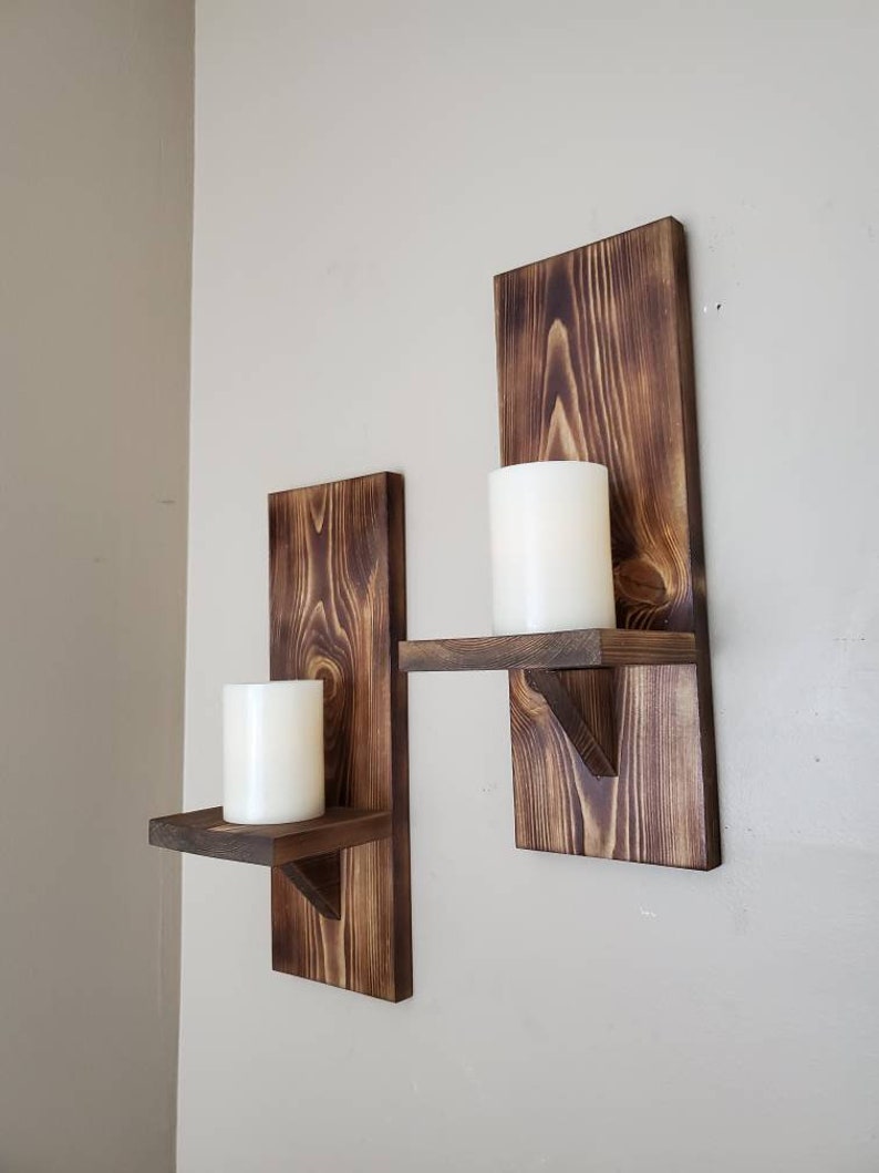 Puede incluir: Dos portavelas de madera r&uacute;stica con estantes. Cada portavelas tiene una forma rectangular y un peque&ntilde;o estante para velas. Los portavelas est&aacute;n te&ntilde;idos de un color marr&oacute;n oscuro y tienen una veta de madera natural.