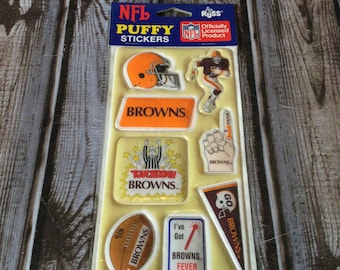 Puede incluir: Una hoja de pegatinas hinchadas con el logotipo del equipo de la NFL Cleveland Browns. Las pegatinas son de varias formas y tamaños, incluyendo una pelota de fútbol, un casco, un jugador y un banderín. Todas las pegatinas son de color marrón y naranja.