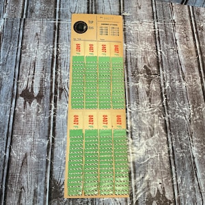 May include: A tan rectangular card featuring eight vertical columns of green pull-tab game tickets. The card is labeled TIP 106, number 8407F, and includes a grid of numbers from 101 to 116. Each green ticket strip has perforated edges.