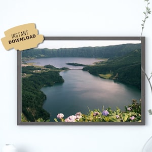 May include: An aerial view of a lake surrounded by lush green hills and trees. The water is a deep blue and the sky is a light blue. There are purple flowers in the foreground.