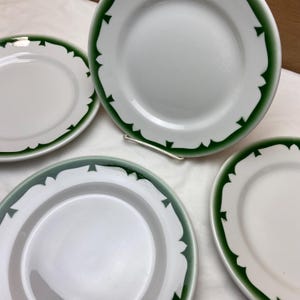 May include: Four white ceramic plates with a green border design. The plates have a simple, elegant design with a green band around the edge.