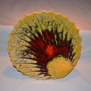 May include: A large ceramic shell-shaped dish with a yellow, red, and black glaze. The dish has a scalloped edge and a raised center.