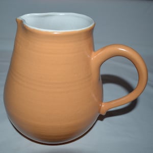 May include: A peach-colored ceramic pitcher with a white interior and a rounded handle.