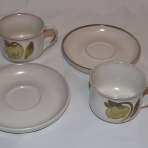 May include: Two white ceramic teacups with brown and green floral designs and matching saucers.