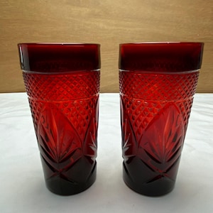 May include: Two ruby red drinking glasses. The glasses have a diamond pattern on the upper portion and a leaf-like design on the lower portion. The rims are a darker shade of red. The glasses are made of glass.