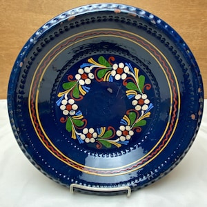 May include: A blue ceramic plate with a white, red, yellow, and green floral design around the rim.