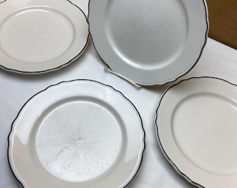 May include: Four white ceramic plates with scalloped edges and a dark blue trim. The plates are arranged on a white surface, showcasing their simple yet elegant design. Ideal for serving meals.