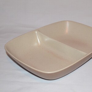 May include: A divided serving dish made of speckled beige ceramic. The dish has a rectangular shape with two equal-sized compartments.