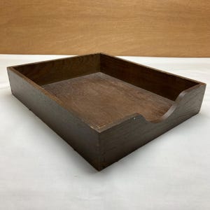 May include: A rectangular dark brown wooden desk tray with a smooth interior base and a curved cutout on the front edge for easy access. The tray features visible finger joint construction at the corners and a natural wood grain texture throughout.