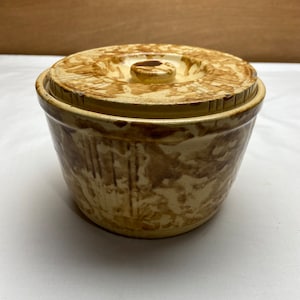 May include: A vintage yellow and brown stoneware crock with a lid. The crock has a decorative pattern and is in good condition.