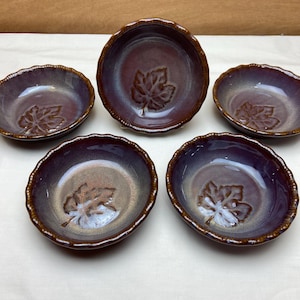 May include: Set of five small purple and brown ceramic bowls with a raised leaf design. The bowls have a scalloped edge.