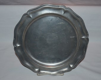 Puede incluir: Un plato de peltre plateado con un borde festoneado. El plato es redondo y tiene una superficie lisa.