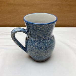 May include: A blue and white speckled ceramic mug with a handle. The mug has a rounded body and a slightly flared rim.