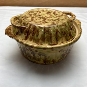 May include: A vintage brown and green glazed ceramic casserole dish with a lid and two handles. The dish has a mottled pattern.
