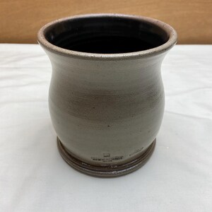 May include: A light gray ceramic vase with a dark gray rim and a slightly flared opening. The vase has a rounded body and a wide base.