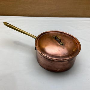 May include: A white ceramic mug with a black handle and the text "But First, Coffee" in a black, handwritten-style font. The mug is on a white surface.